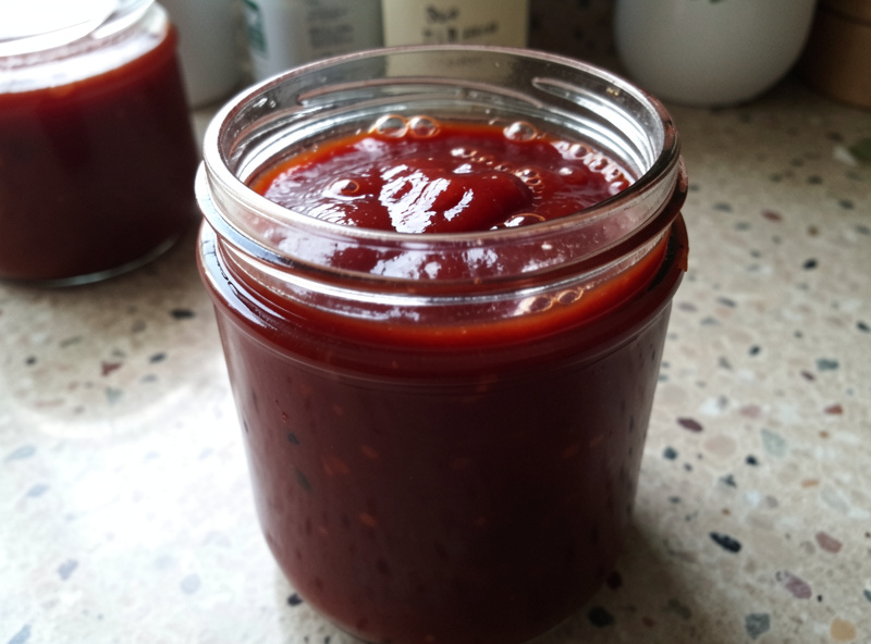 Rich dark red homemade fermented ketchup in a glass jar with bubbles at the surface