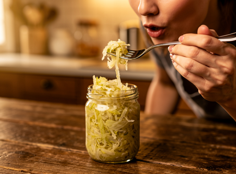 A person tasting a forkful of sauerkraut from a jar to check the sourness