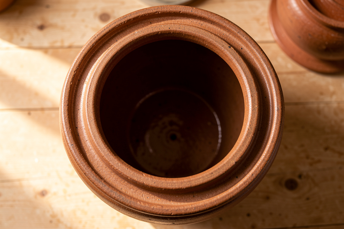 Top-down view of a water-sealed stoneware fermentation crock with lid removed, showing the water moat channel