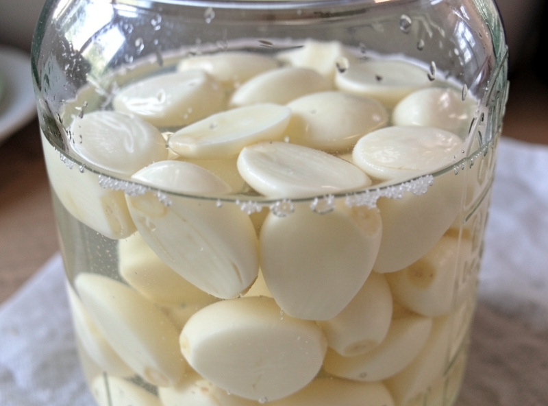 Peeled garlic cloves submerged in a clear saturated salt brine inside a glass jar