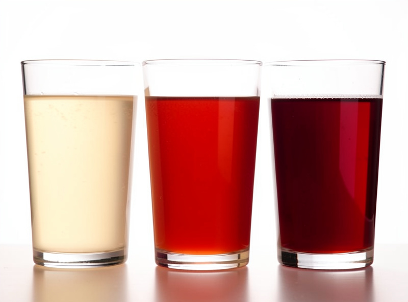 Three glasses of shrub soda side by side ranging from pale to deep ruby showing different sugar and dilution levels, backlit