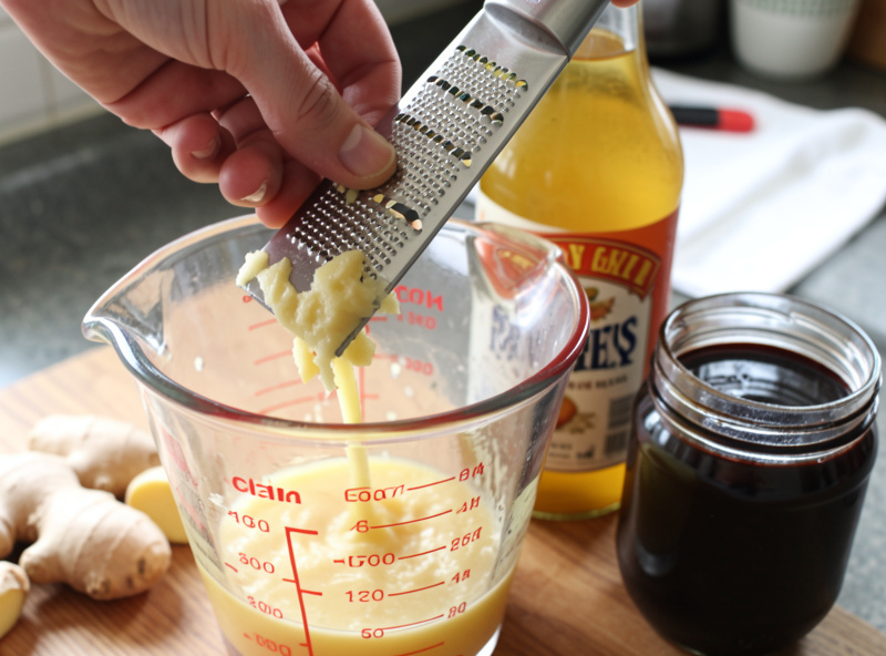 Fresh ginger grated on a microplane over a measuring jug with apple cider vinegar and a jar of dark molasses beside it