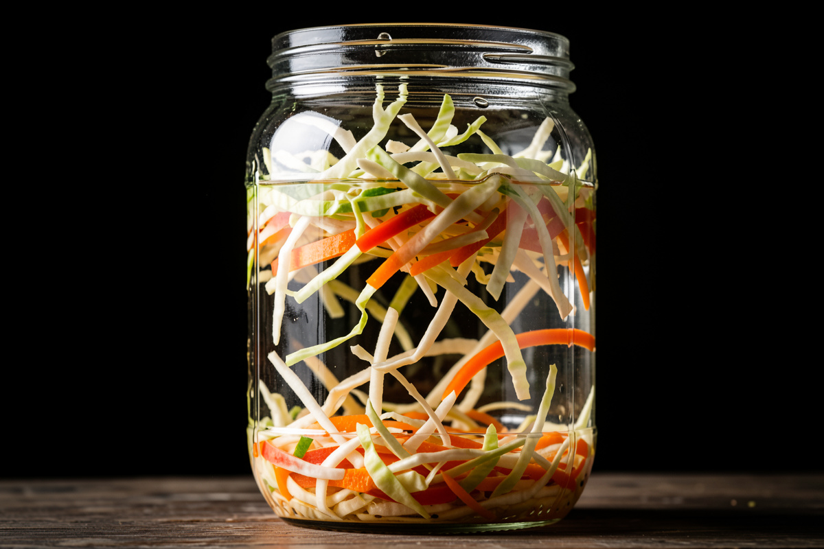 Shredded vegetables floating above the brine line inside a glass fermentation jar